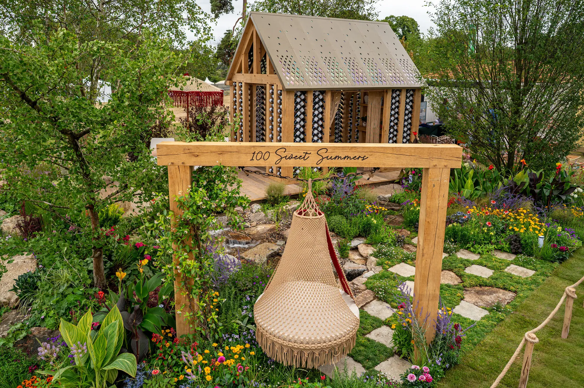 Overview of the 100 Sweet Summers garden showing the macramé swing, water feature, stepping-stone path and oak building