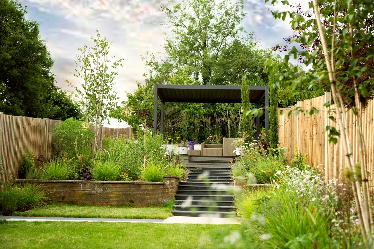 The terraced garden seen from the lower lawn, with steps rising through the brick retaining wall to the steel pergola and its seating