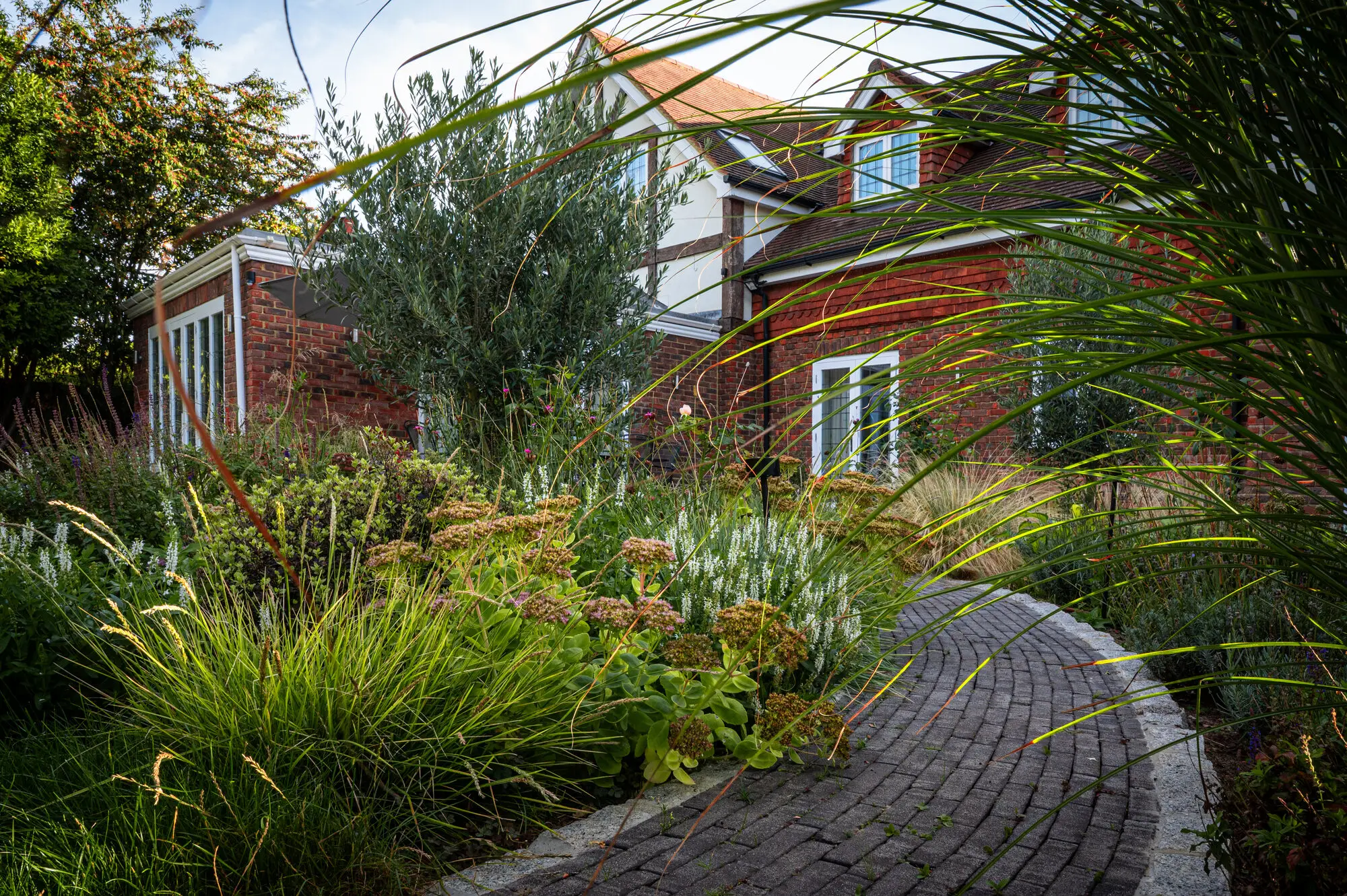 The curving brick path running past sedum, white salvias and grasses towards the orangery