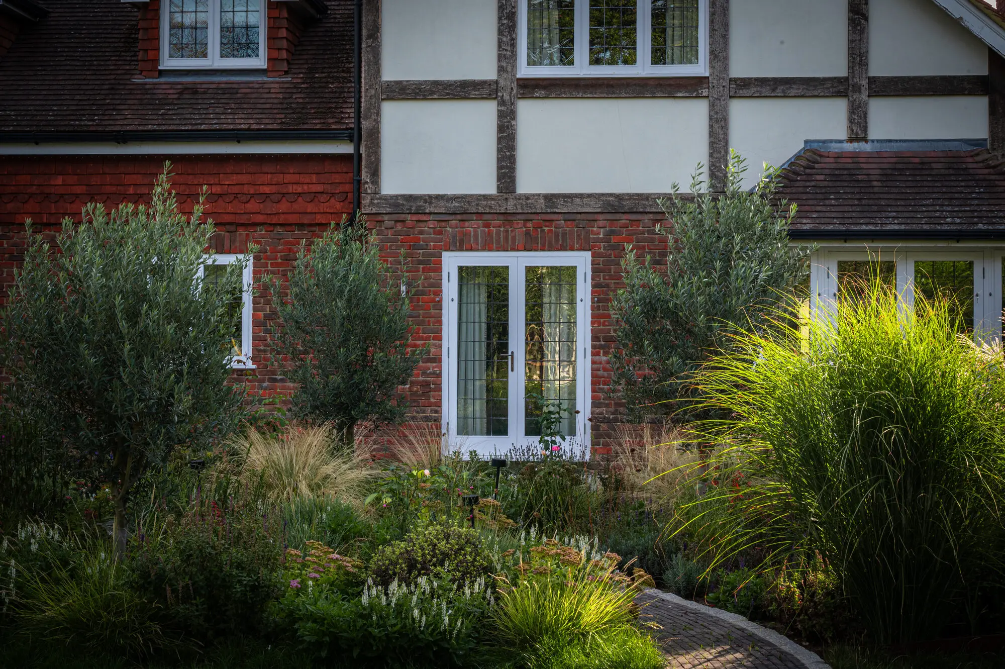 Ornamental grasses and olive trees in front of the timber-framed house