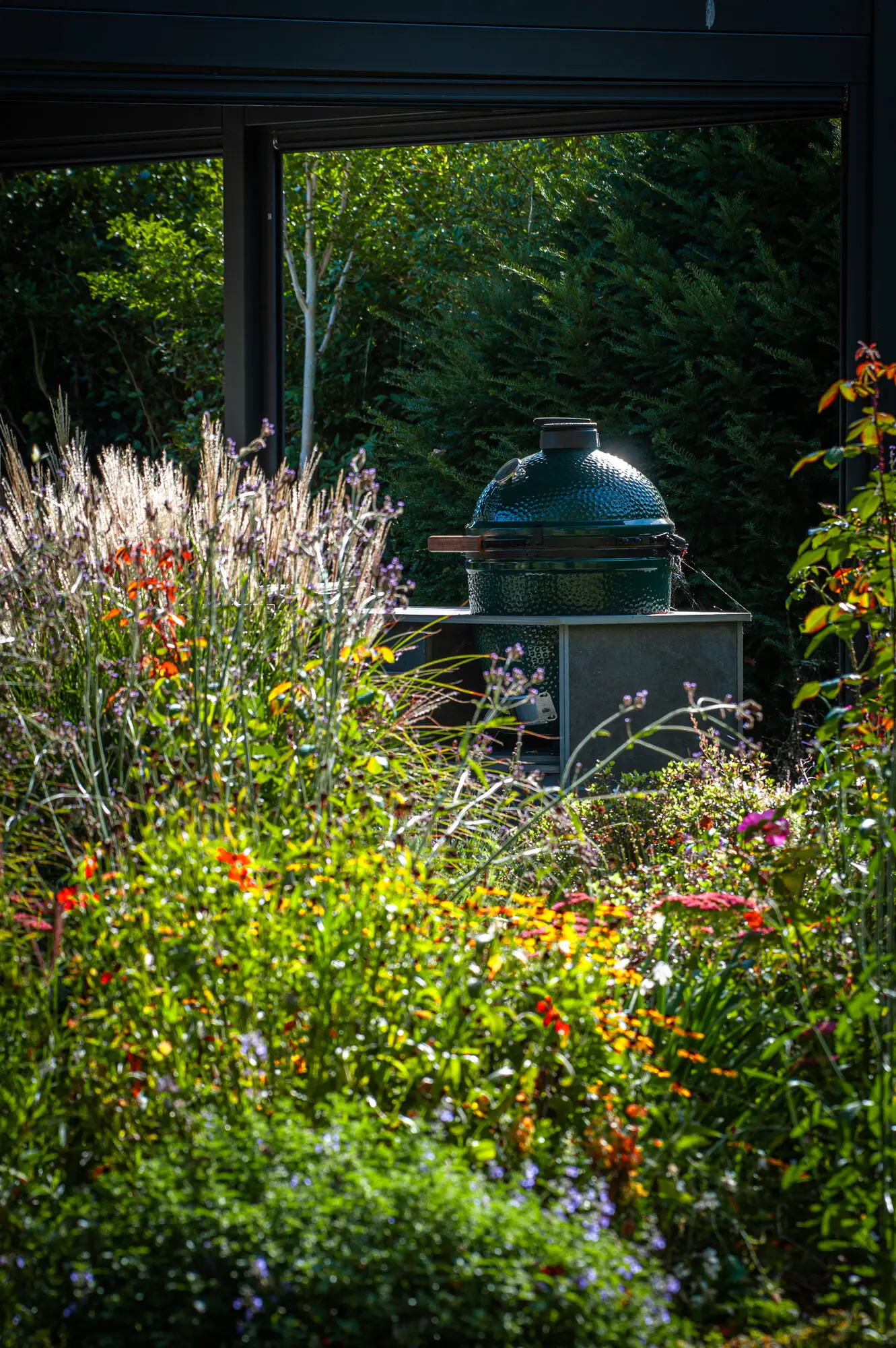 The outdoor kitchen and Big Green Egg under the pergola, behind grasses and flowering perennials