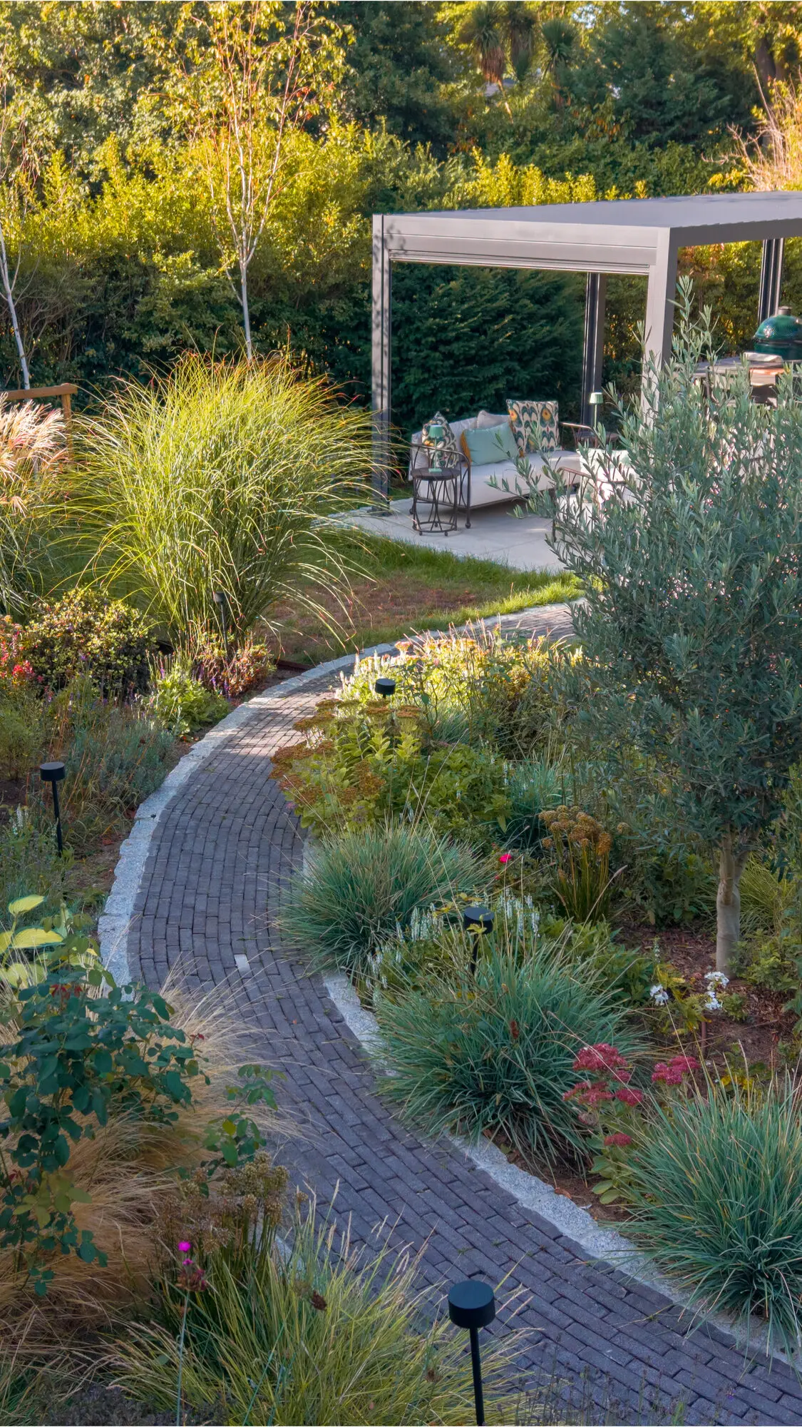 The brick path curving through grasses and perennials to the pergola, seen from above the border