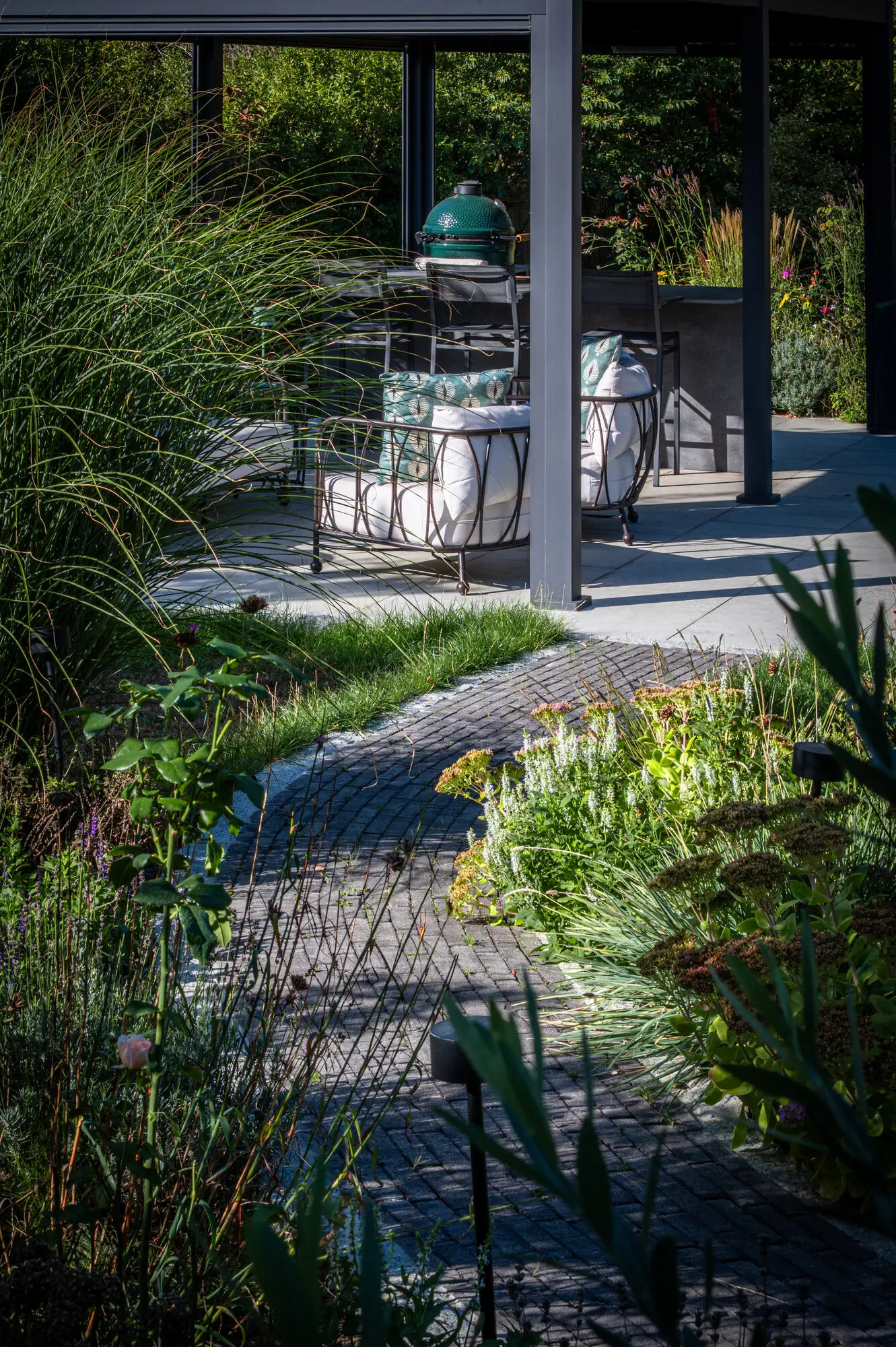 The pergola with its seating and outdoor kitchen at the end of the brick path