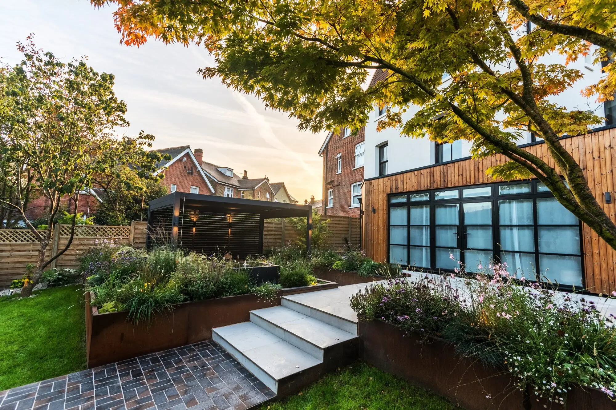 Pale stone steps between corten steel planters leading up to the terrace, with gaura and grasses flowering beside them