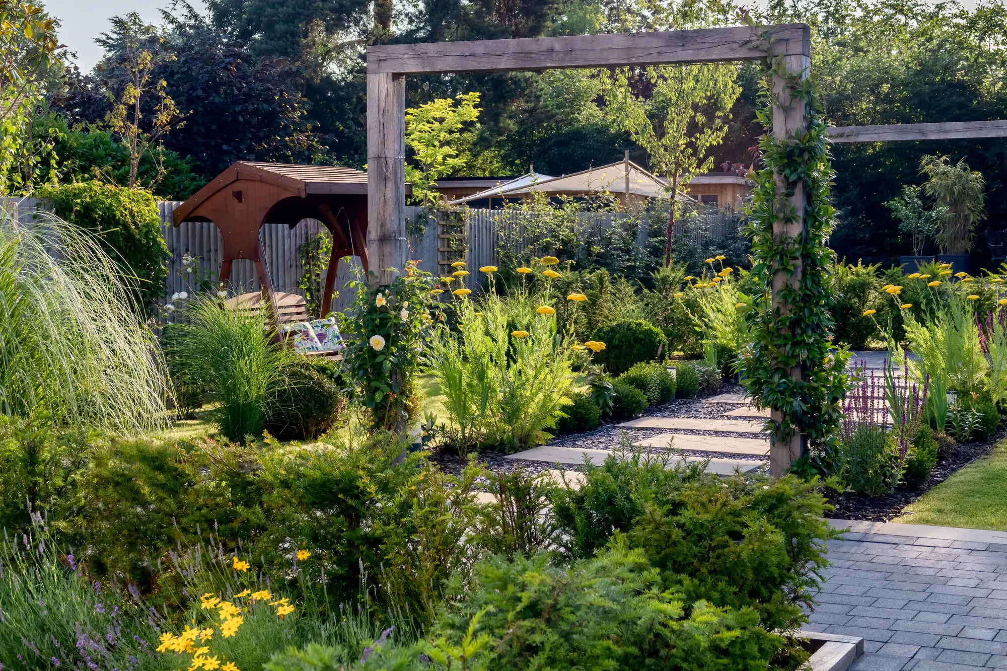 A timber arch over the path of the Garden Hideaway, with layered perennials, clipped box and grasses on both sides