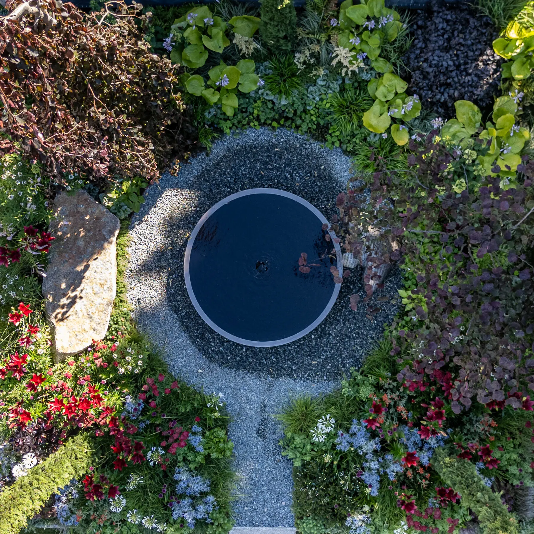 The round reflecting pool at the centre of the garden, seen from above, ringed by gravel and layered planting