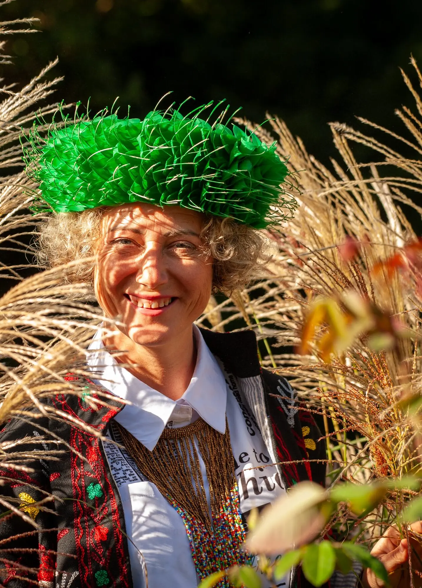 Kitti Kovacs in a green hat smiling among tall ornamental grasses