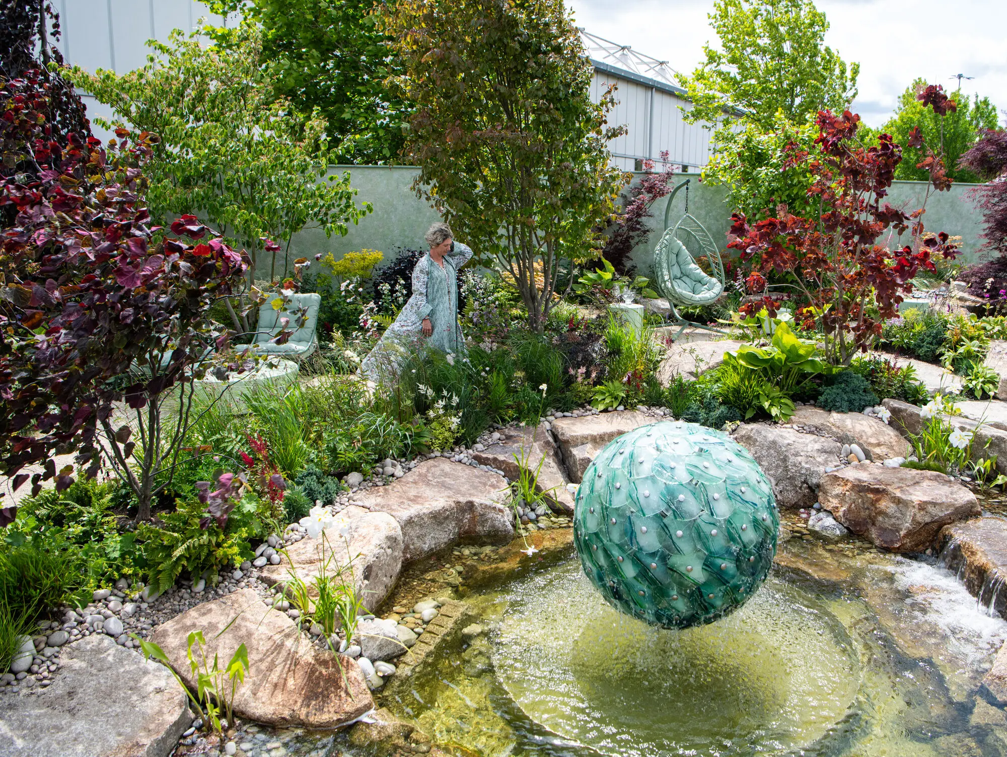 Kitti Kovacs walking through the planting of the Reflective Retreat, beyond the green glass sphere fountain