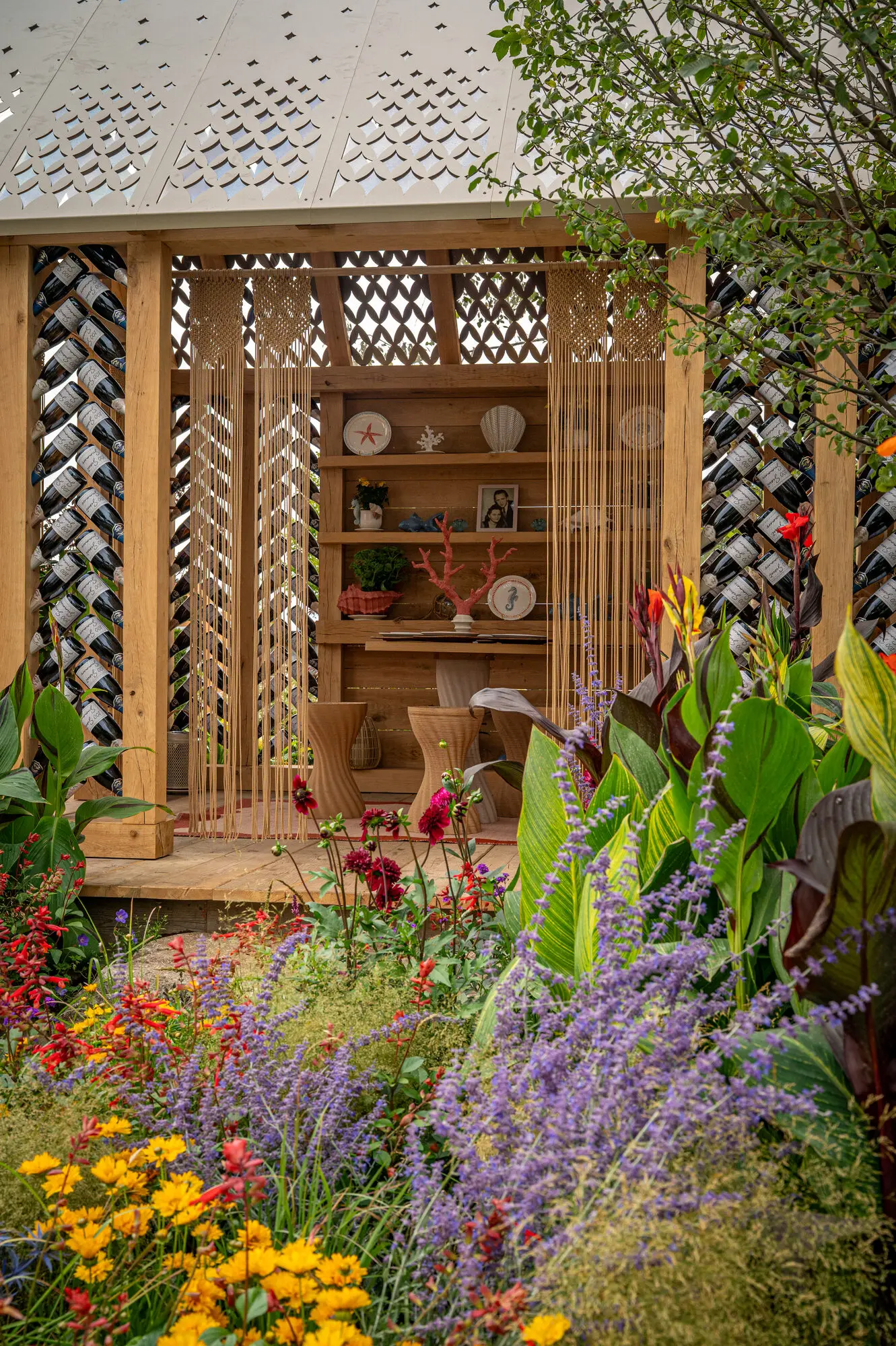 Oak garden building with recycled wine bottle walls, macramé details and colourful surrounding planting