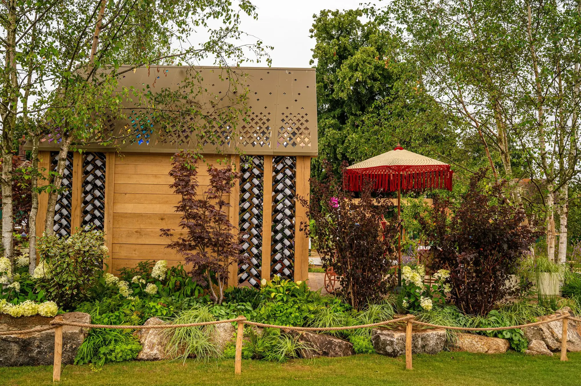Sustainable oak garden building with recycled wine bottle walls and handmade macramé parasol