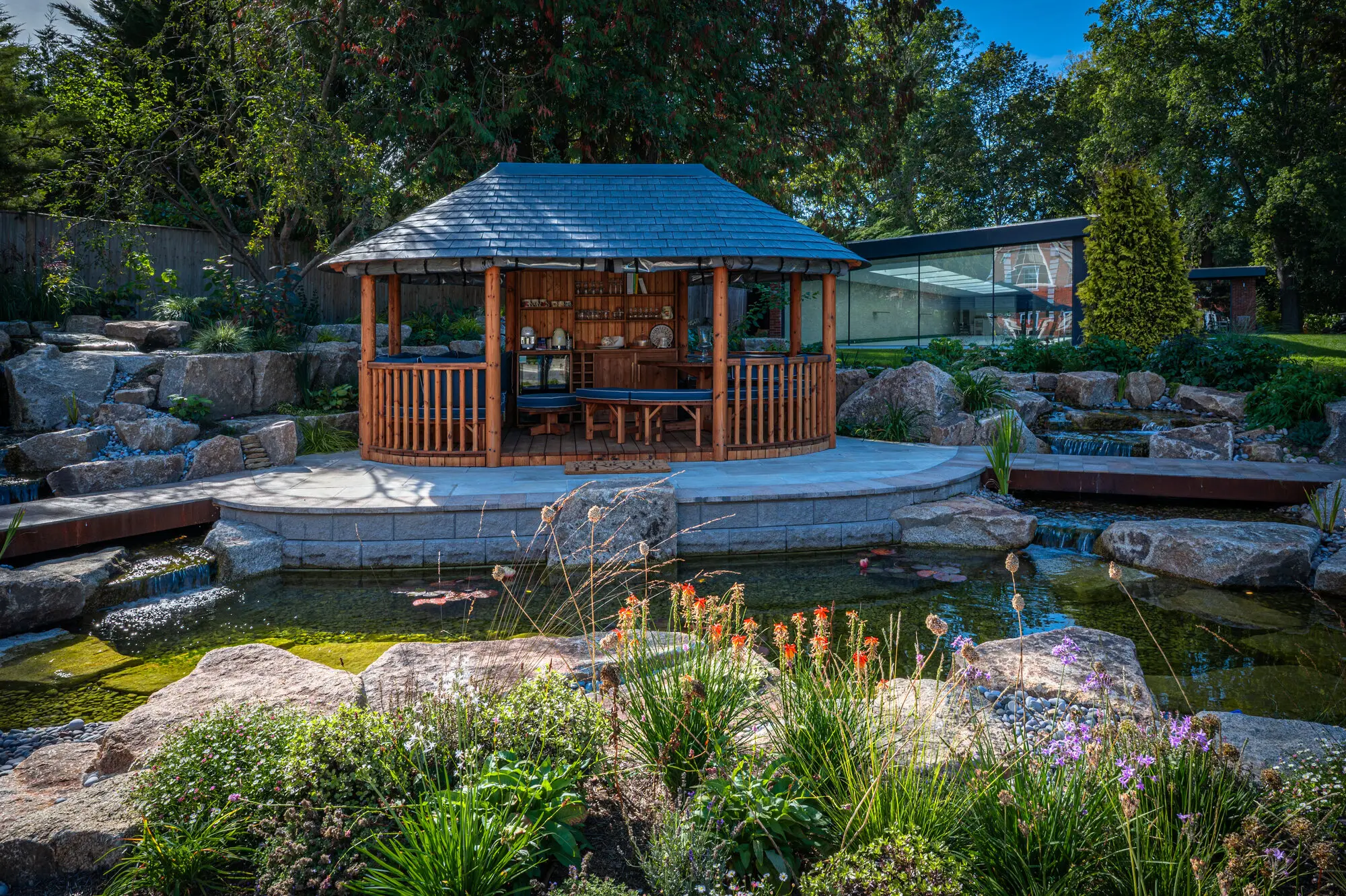 The Breeze House on its island seen across the pond, with red hot pokers and grasses at the water's edge