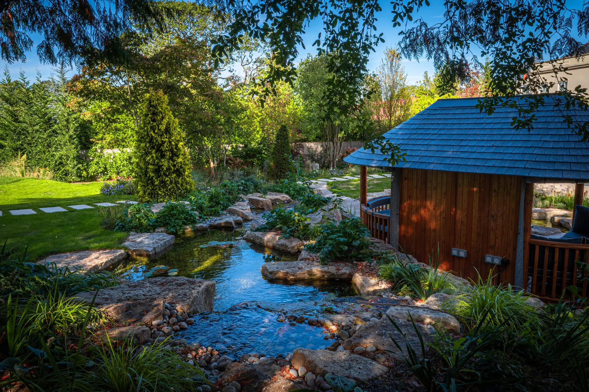 The Breeze House on its island, with a stream running between granite stepping stones and planting into the ponds