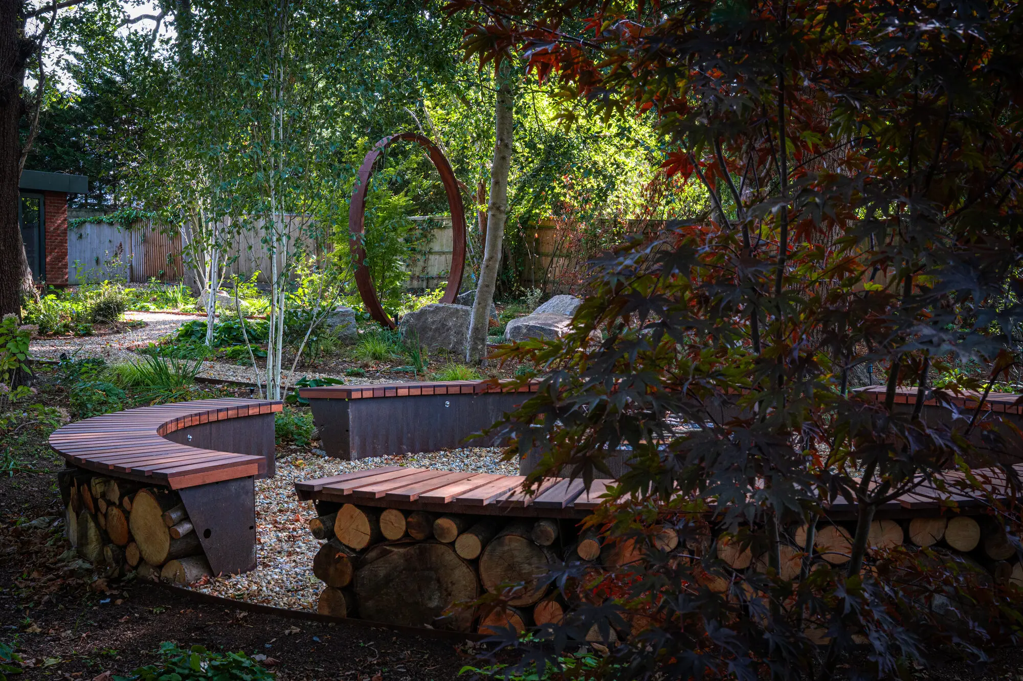 The benches around the fire pit, with the moon gate among the birches beyond