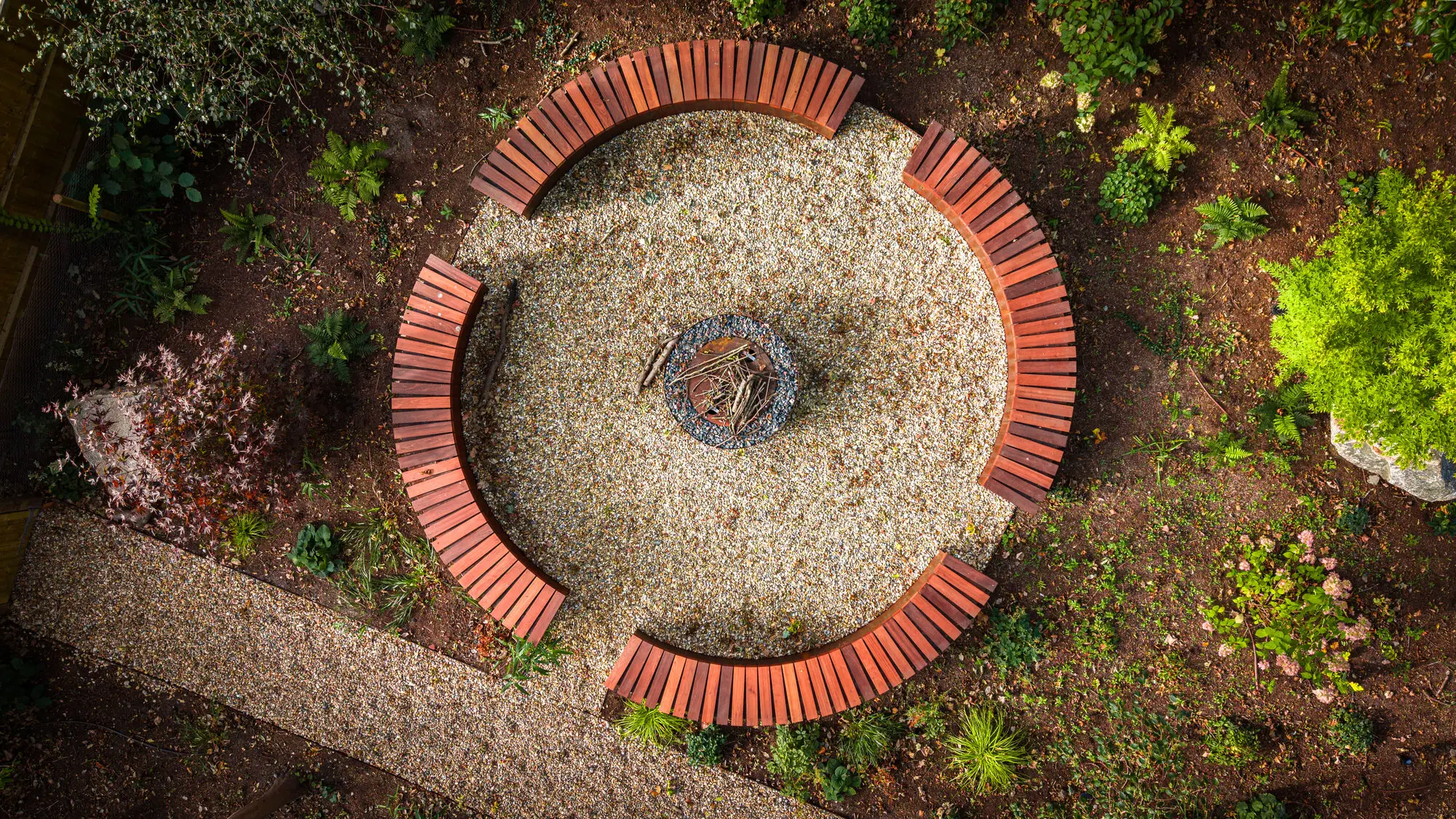 The sunken fire pit from above, ringed by curved timber benches in the woodland garden