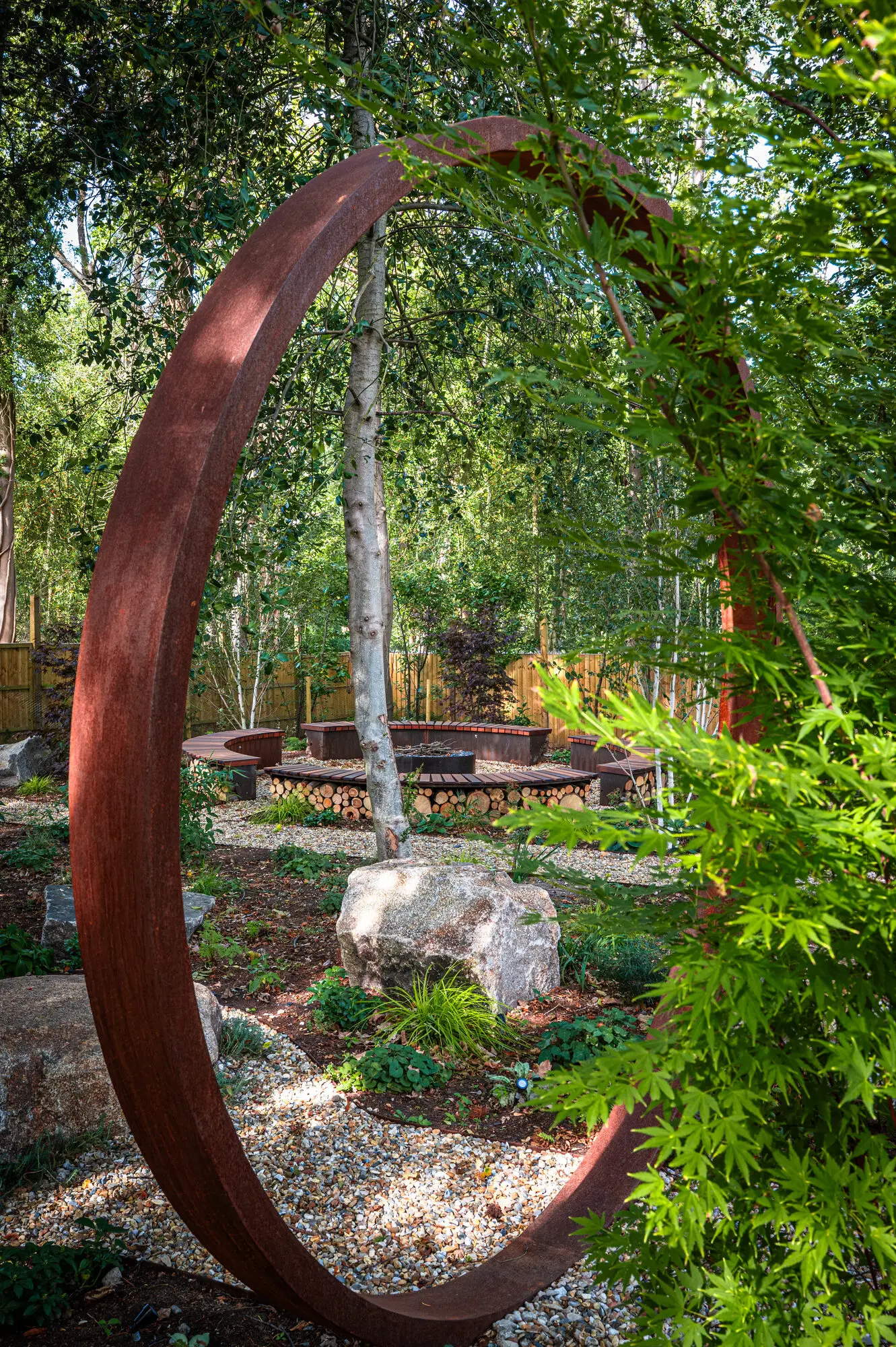 Looking through the corten steel moon gate past birches to the fire pit