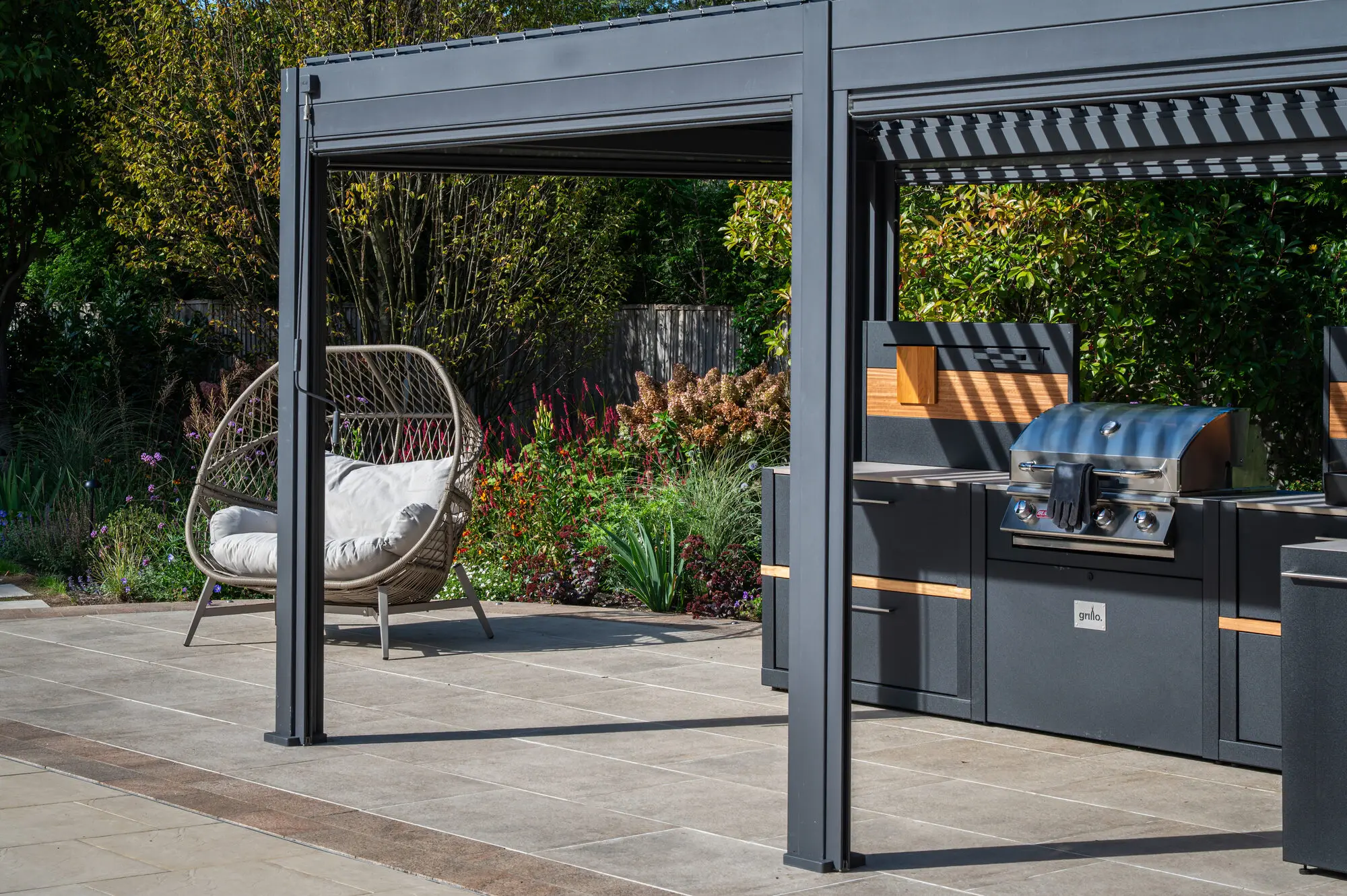 The outdoor kitchen under the pergola, with a hanging egg chair beside it