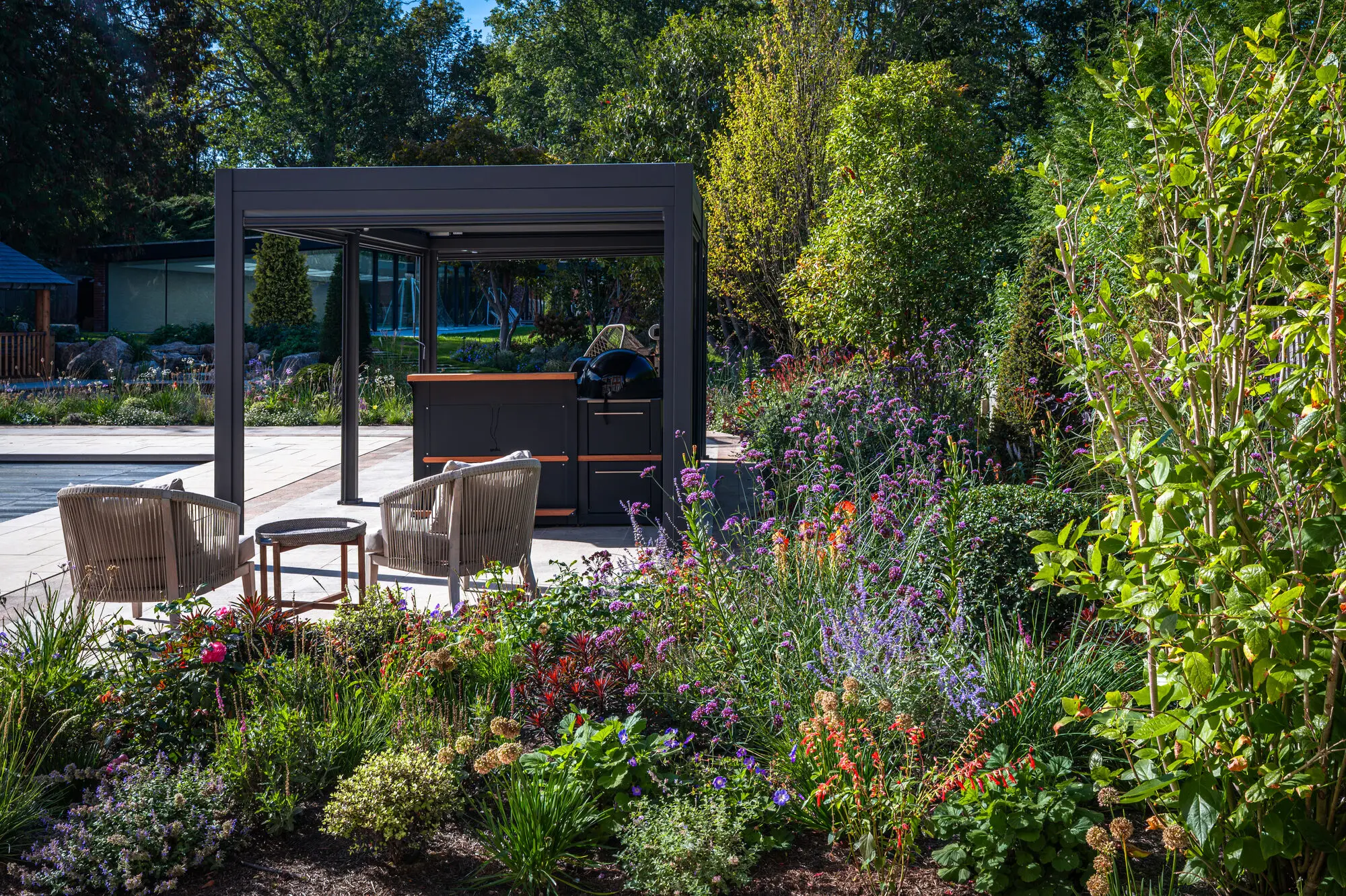 The pergola and outdoor kitchen beside the pool terrace, behind a deep border of salvias, verbena and roses