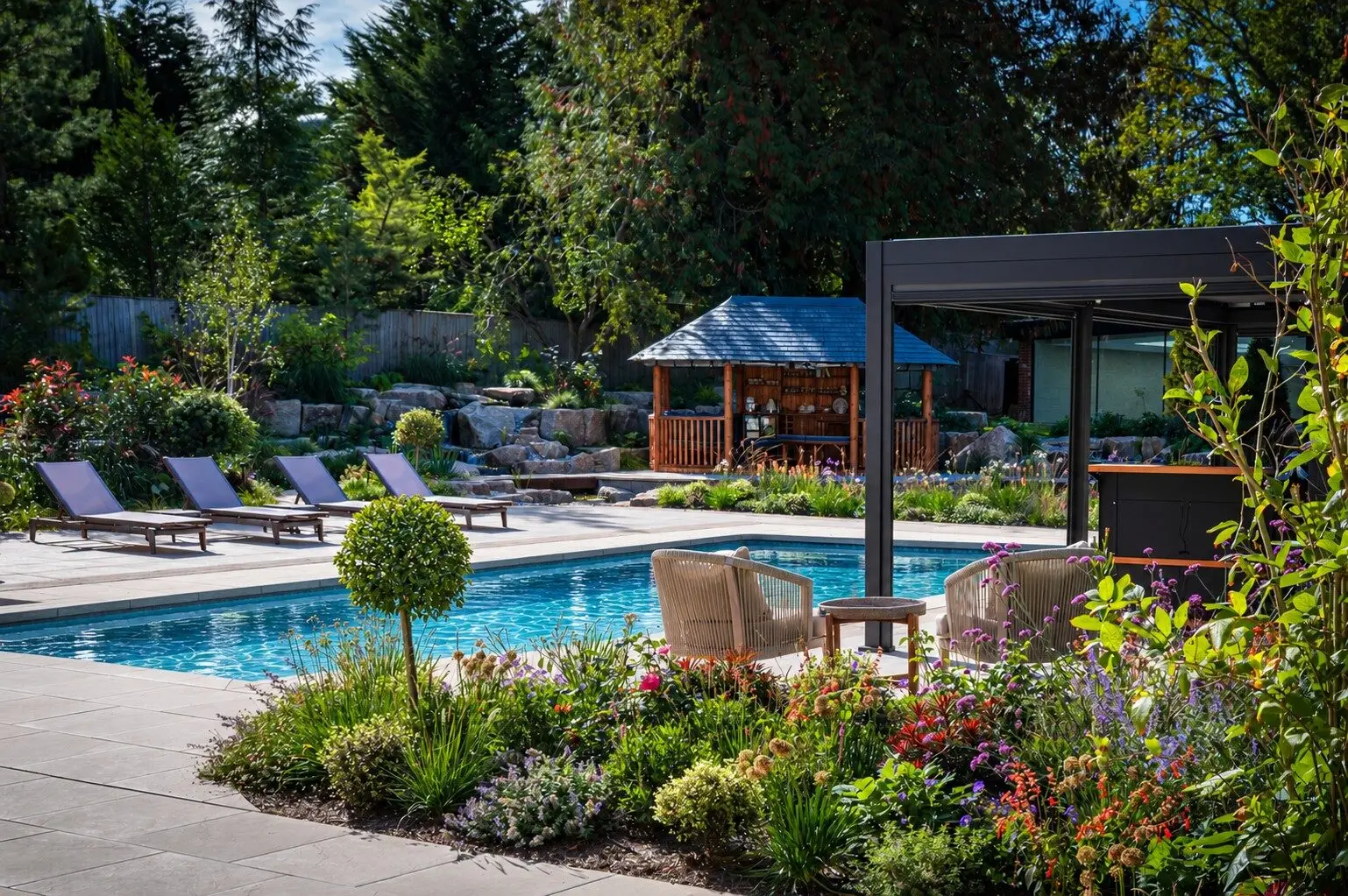 The pool terrace with four sun loungers, the pergola and outdoor kitchen, and the Breeze House among the granite waterfalls behind
