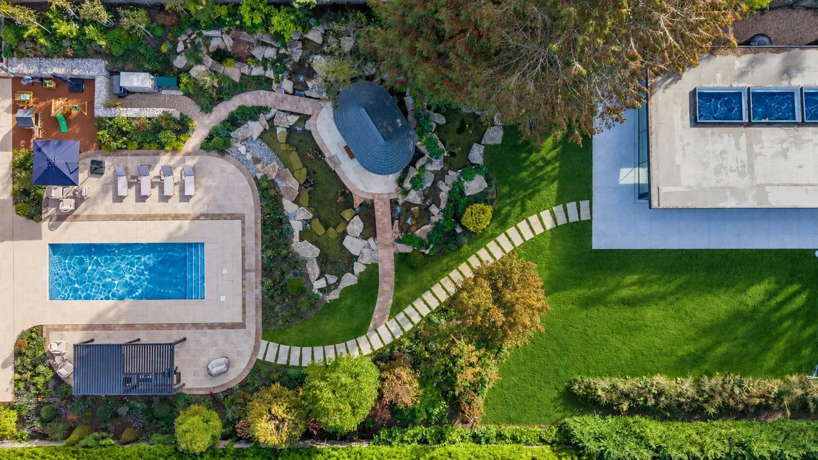 The whole garden from above: the pool terrace and pergola, the Breeze House among the granite ponds, the stepping-stone path across the lawn to the pool house
